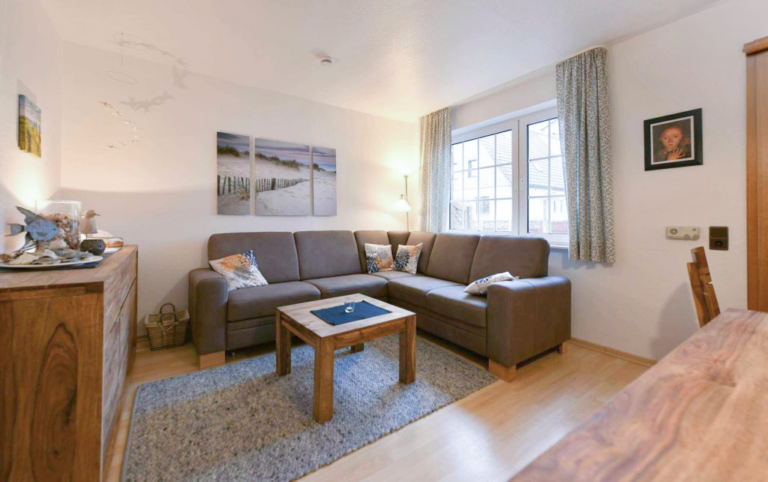 Gemütliches Wohnzimmer mit Ecksofa, Holzmöbeln und maritimer Dekoration in der modernen Ferienwohnung Boje 27-5.