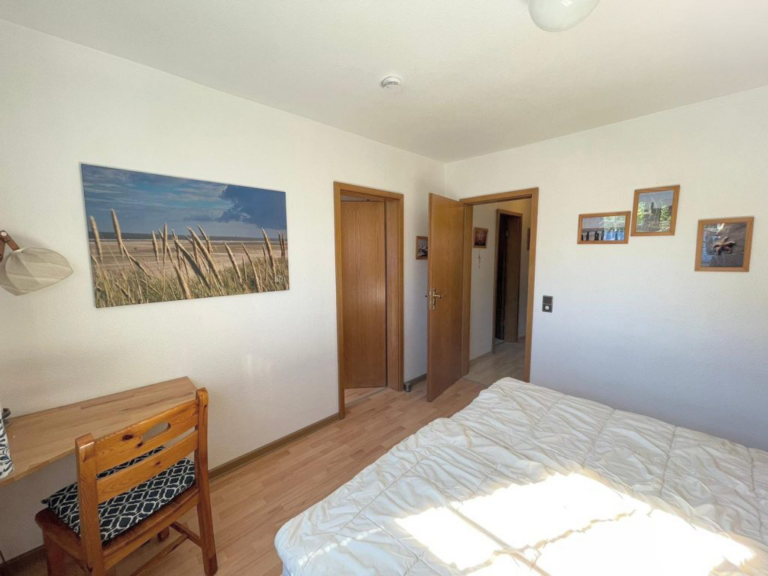 Helles Schlafzimmer mit Doppelbett, Holzmöbeln und maritimer Wanddekoration im Appartement Boje 27-5.